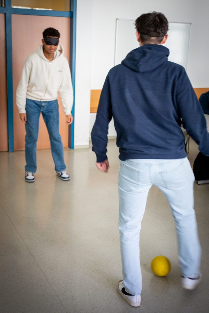 Zwei Schüler versuchen mit einem Klingelball mit verdeckten Augen gegeneinander Fußball zu spielen
