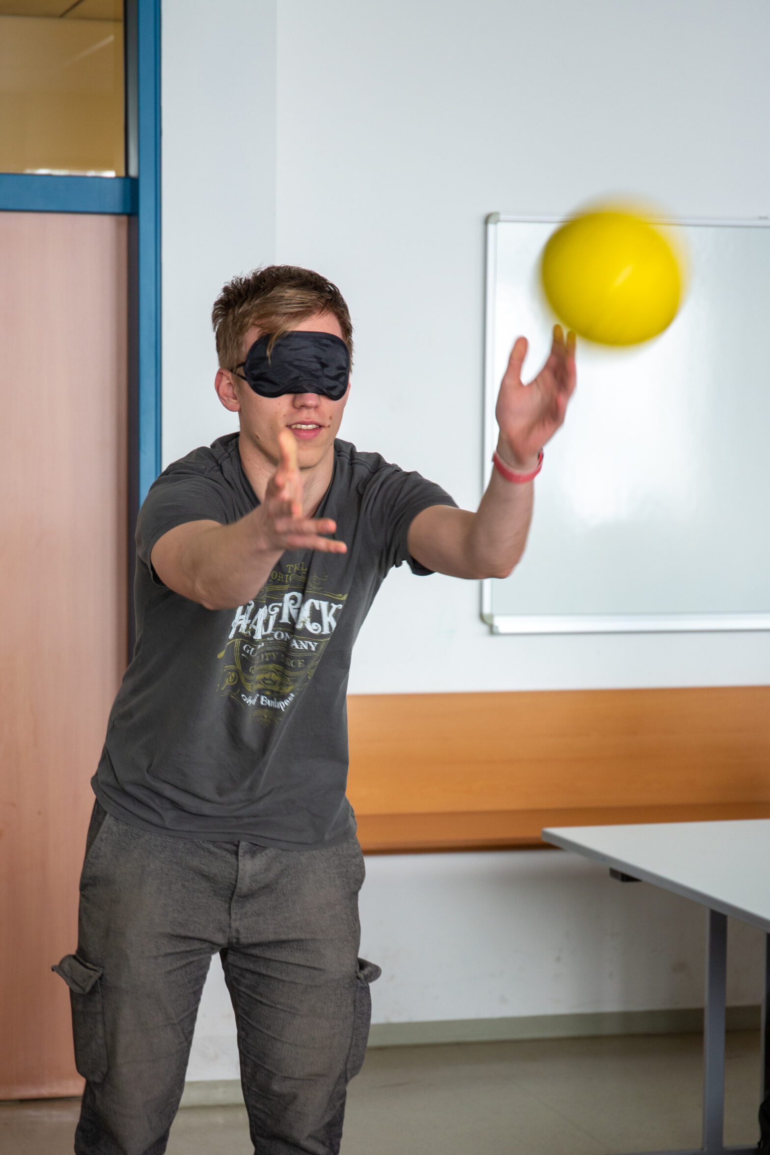 Uczeń niedowidzący próbuje złapać rzuconą piłkę z zasłoniętymi oczami